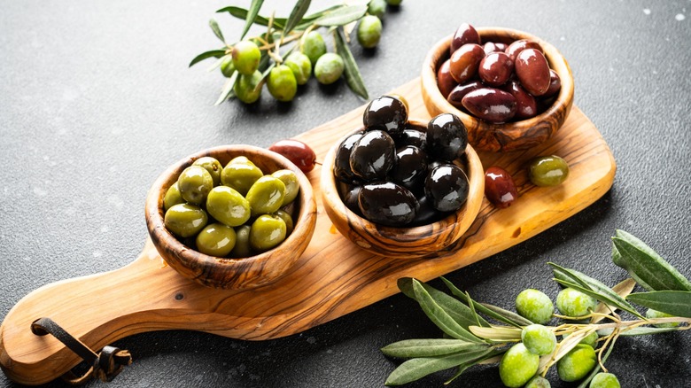 Assortment of whole olives in small containers placed on wooden cutting board